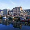 A row of boats on the water, and behind are the shops and restaurants on Plymouth's Barbican