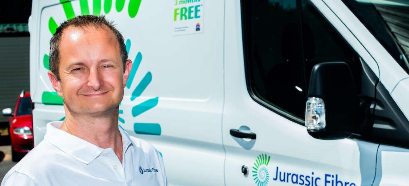 Matt Baker of Jurassic Fibre smiling at the camera, with a branded Jurassic Fibre van behind him