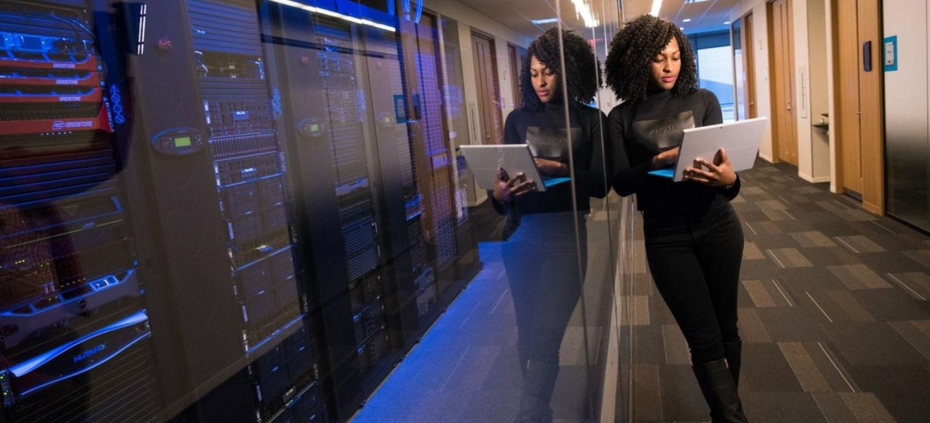 A woman using a laptop next to a large server room