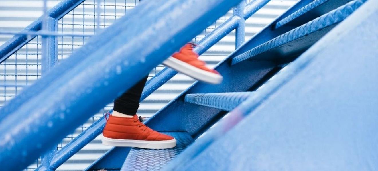 A close up of a person's orange trainers walking up blue metal stairs