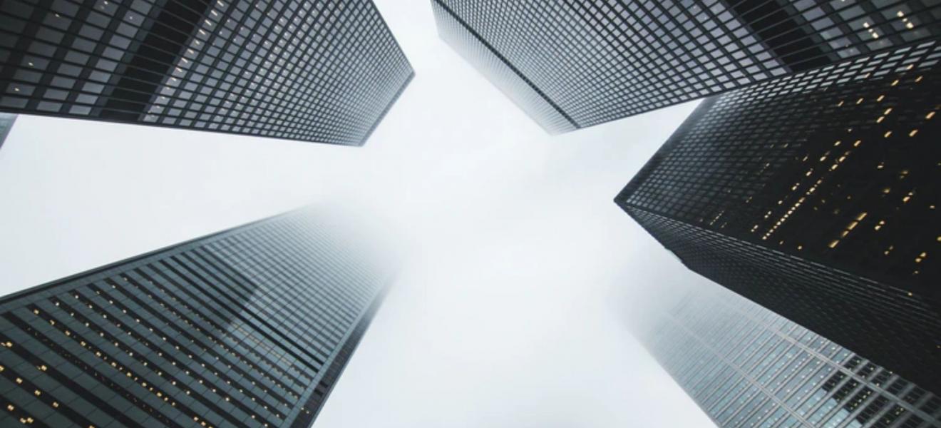 A grey shot taken upwards at some high rise buildings in a financial district. 
