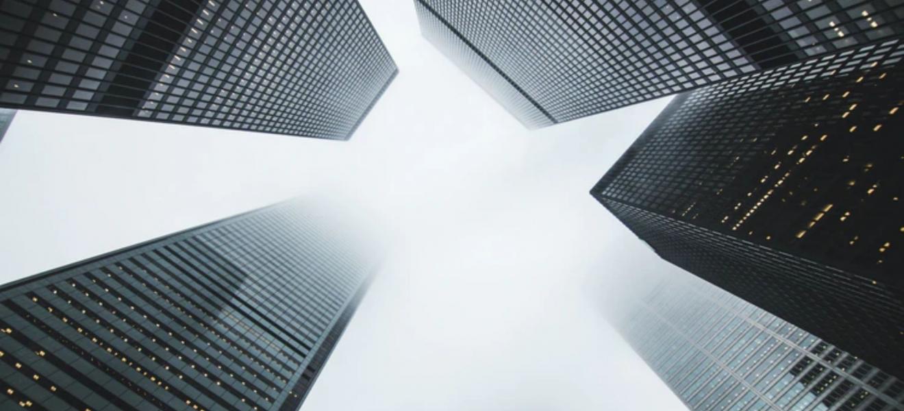 A grey shot taken upwards at some high rise buildings in a financial district.