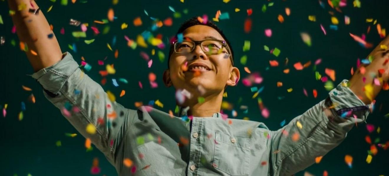 A smartly dressed person throwing confetti in the air against a black background