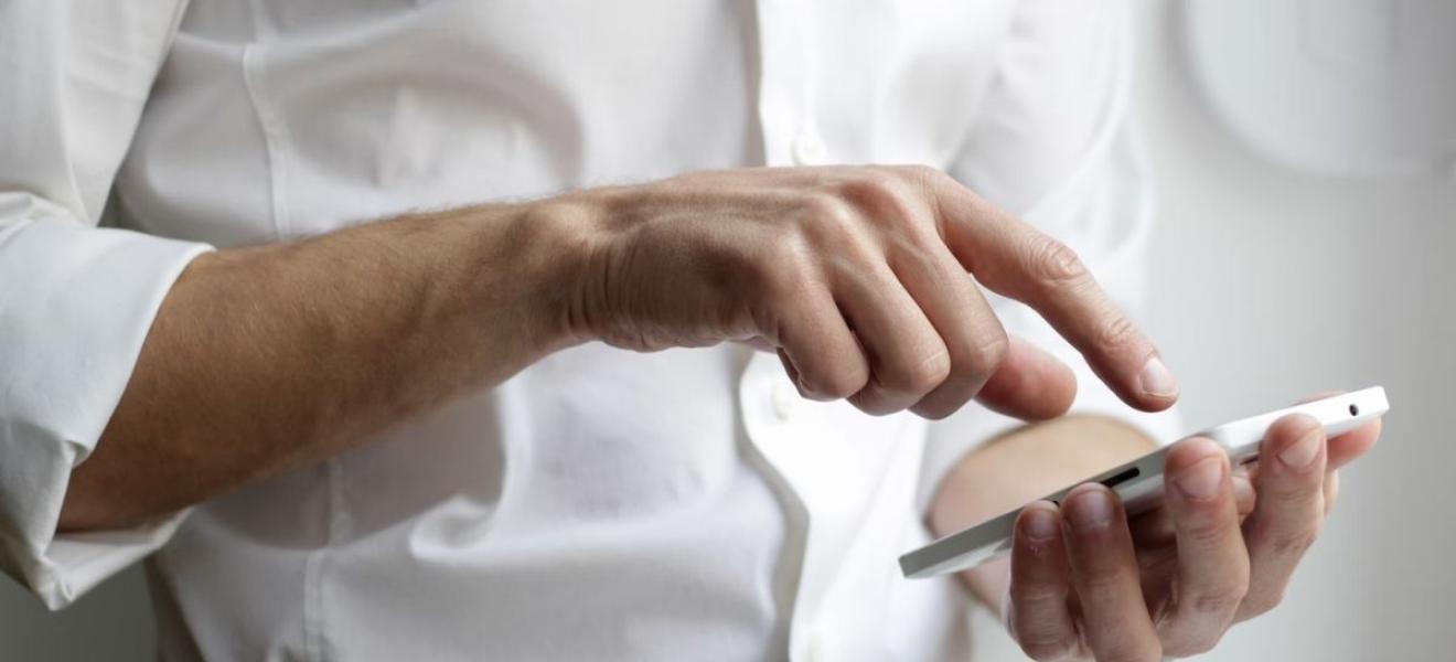 A man wearing a white shirt, using a mobile smartphone