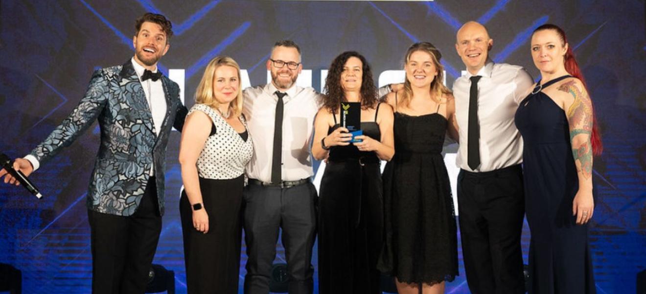 (L-R) Awards host, Joel Dommett with Jaye Cowle, Mike Sharpe, Steph Iles, Harriet Barter, Tom Cowle and sponsor representative. The Launch team on stage receiving an award