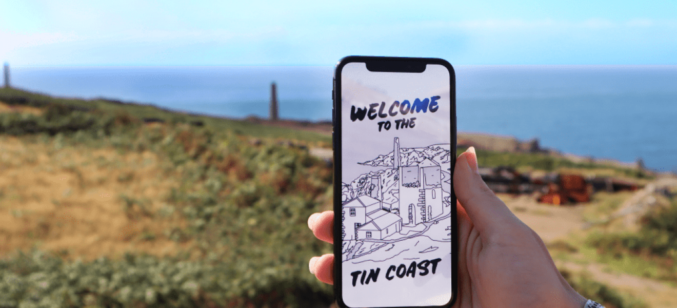 A hand holds a phone showing the XplorTINCOAST landing page. There is a coastal background.