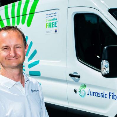 Matt Baker of Jurassic Fibre smiling at the camera, with a branded Jurassic Fibre van behind him