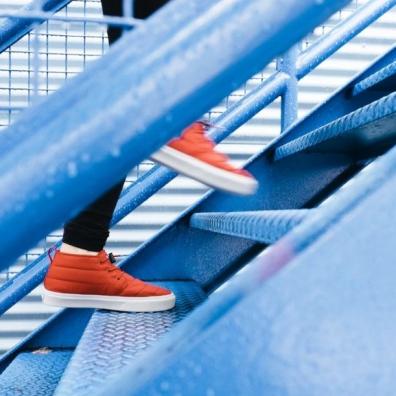 A close up of a person's orange trainers walking up blue metal stairs