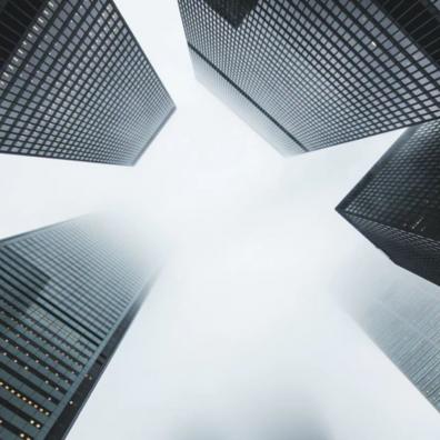 A grey shot taken upwards at some high rise buildings in a financial district. 