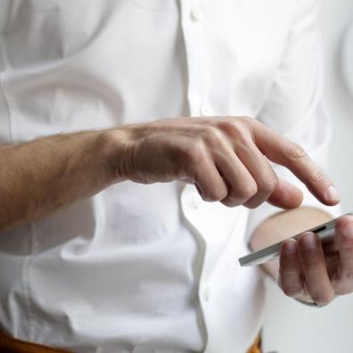 A man wearing a white shirt, using a mobile smartphone